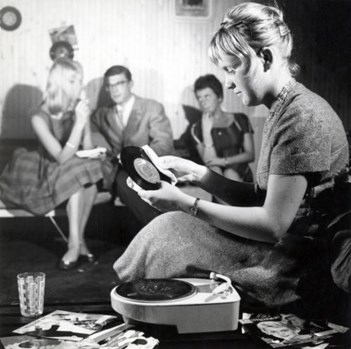 Teenager meisje stoft een single af tijdens het plaatjes draaien op een eenvoudige grammofoon (platenspeler  pick up), jaren &#39;60.